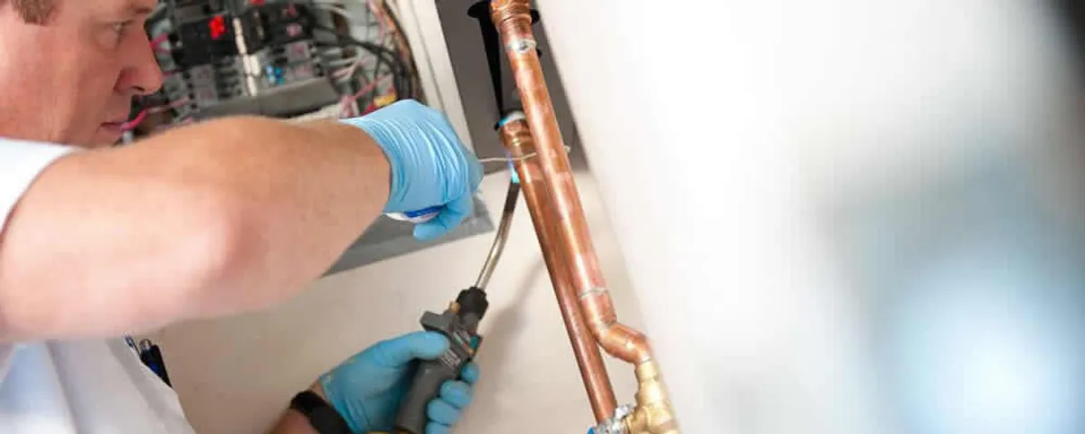 Water heater repair technician testing copper pipe connections and controls in San Antonio, TX
